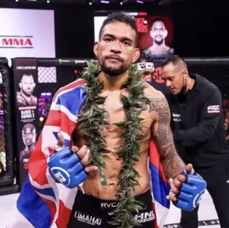 Yancy Medeiros standing victorious in the MMA ring, draped in a Hawaiian flag and lei, showcasing strength and resilience.